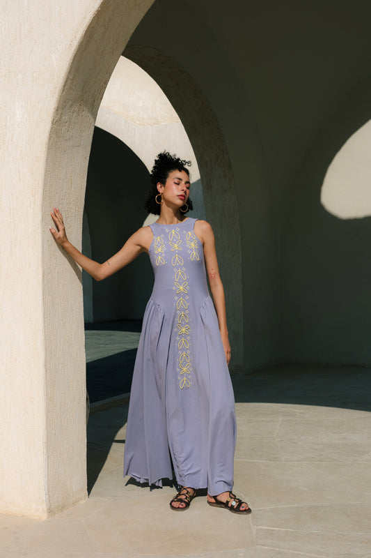 Woman in a light purple dress with embroidery standing in front of a stone archway.