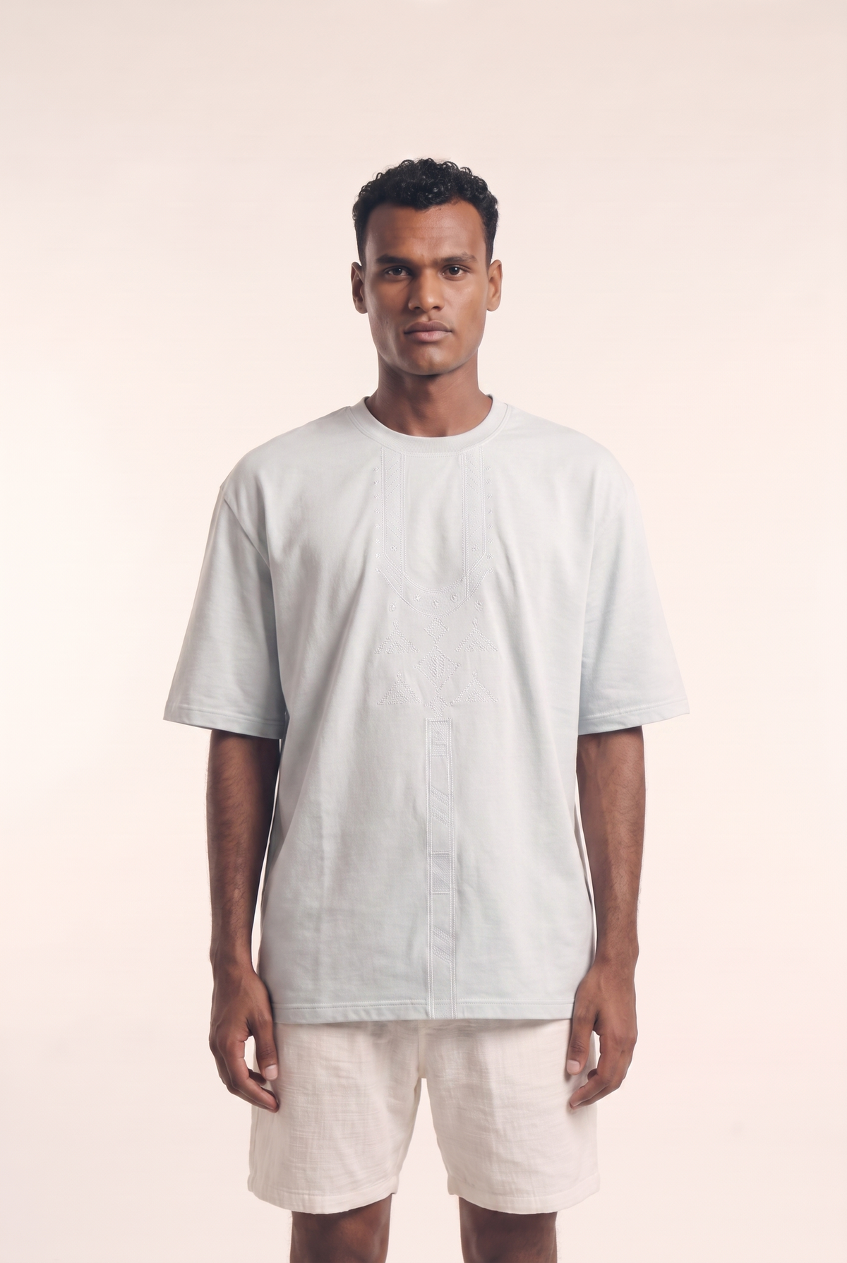 Light blue t-shirt with white Nubian necklace embroidery at the neckline, front view.