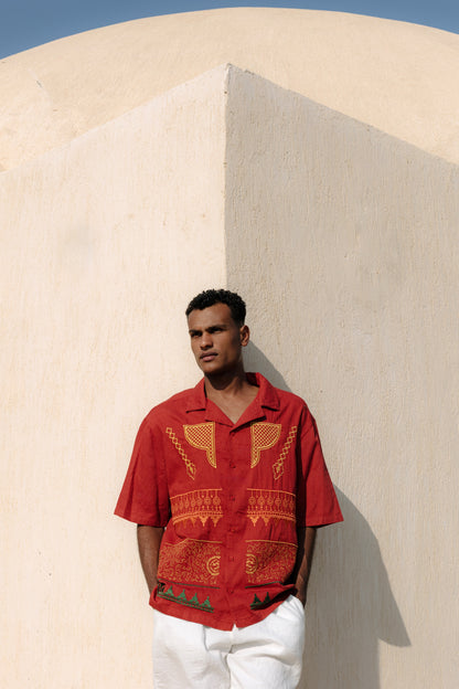 Man wearing a maroon nubian patterned shirt against a beige wall