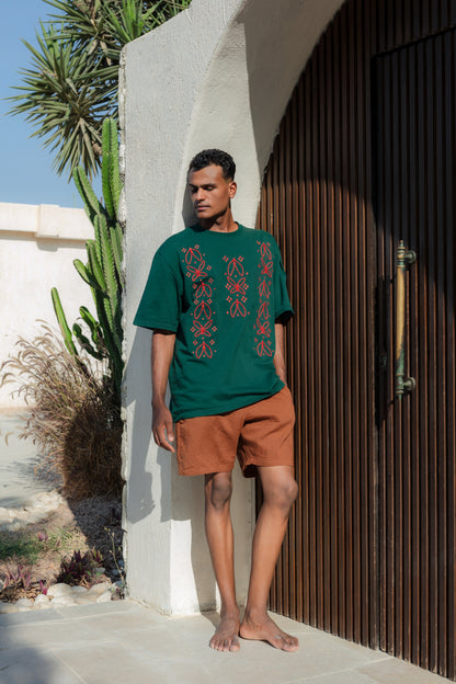 Man wearing a green embroidered t-shirt and brown shorts standing outdoors.