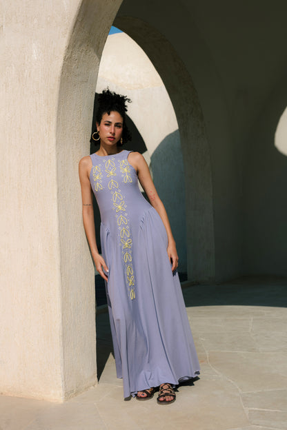 Woman in a long, light purple dress with floral embroidery standing in an archway.
